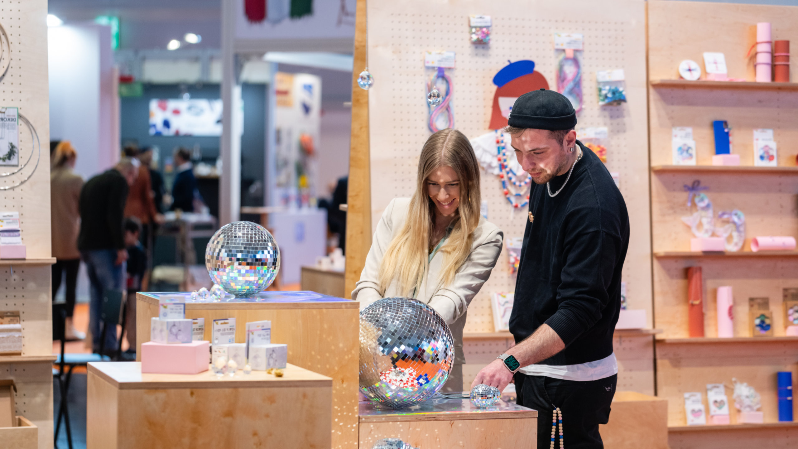 eine junge Frau und ein junger Mann an einem Stand mit Diskokugeln auf der Creativeworld