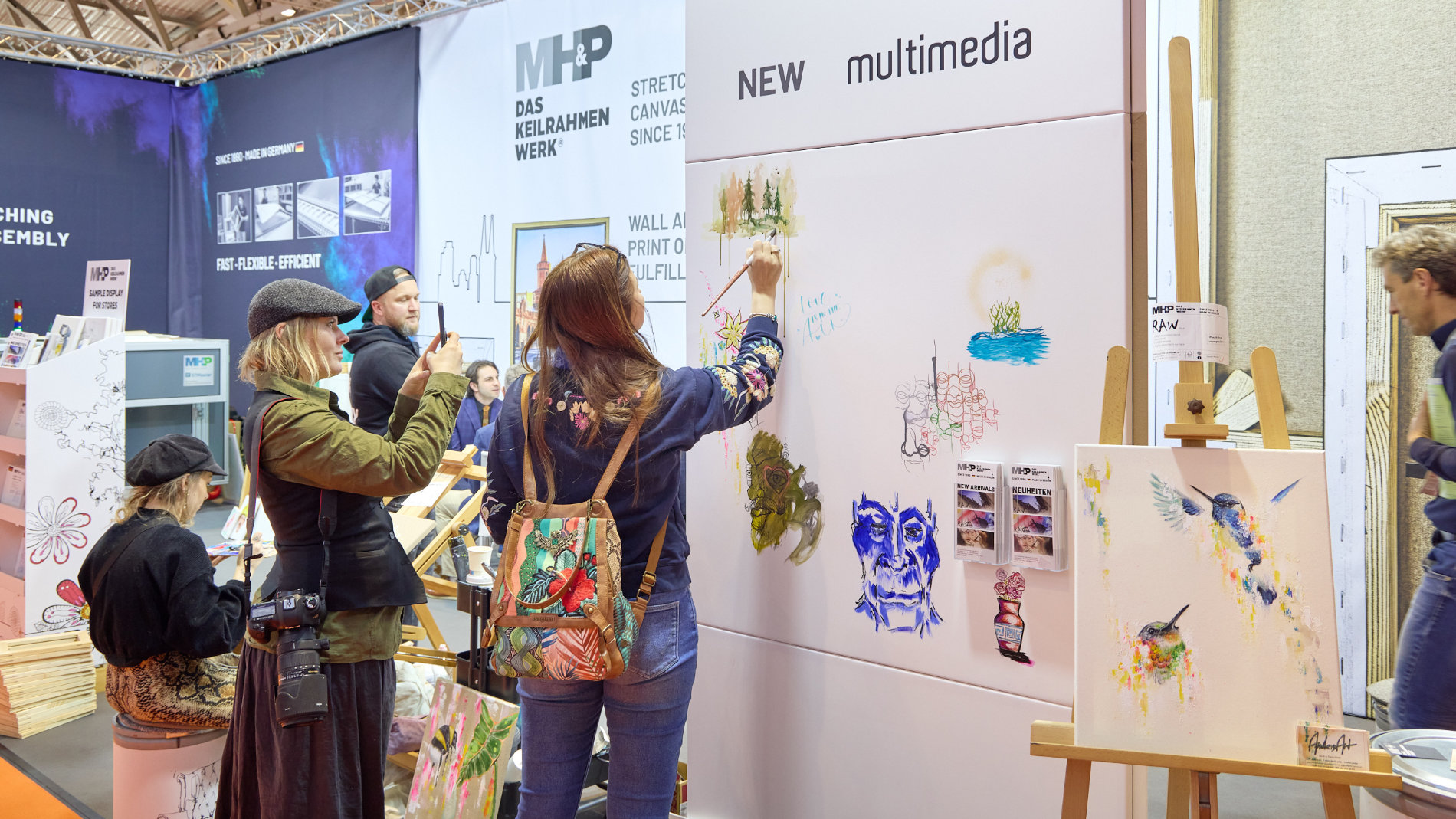 Messebesucher und Künstler malen an einem Messestand auf der Creativeworld